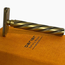 Load image into Gallery viewer, A vintage-style safety razor with a twisted handle in a brushed brass/gold finish, resting on top of its textured orange packaging box. The box features the brand name 'Darker' and the text 'Safety Razor Since 1979'.